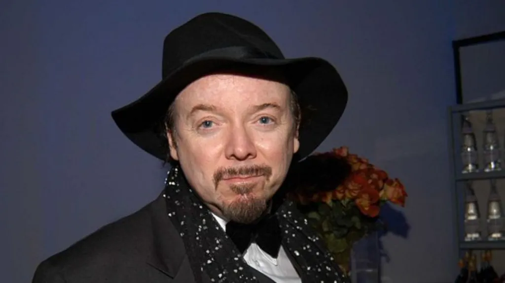 Bud Cort wearing a black hat and black suit