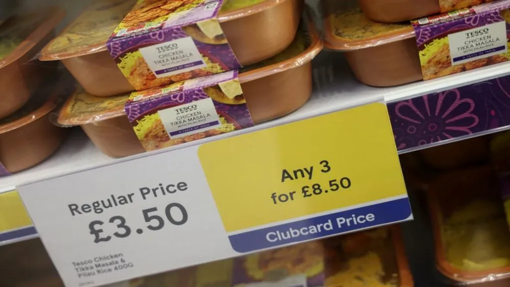 Chicken tikka masala ready meals on a shelf next to a sign offering discount deals inside a Tesco supermarket in Manchester.