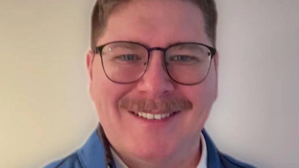 A head shot of James Richardson, who is smiling. He has glasses and a mustache