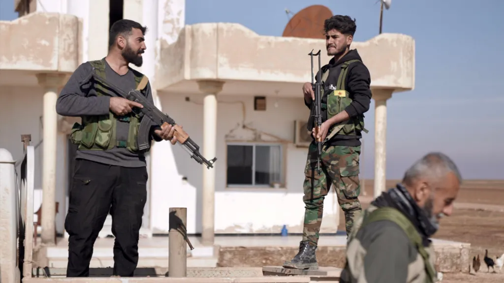 Kurdish soldiers stand on a wall with their weapons in hand