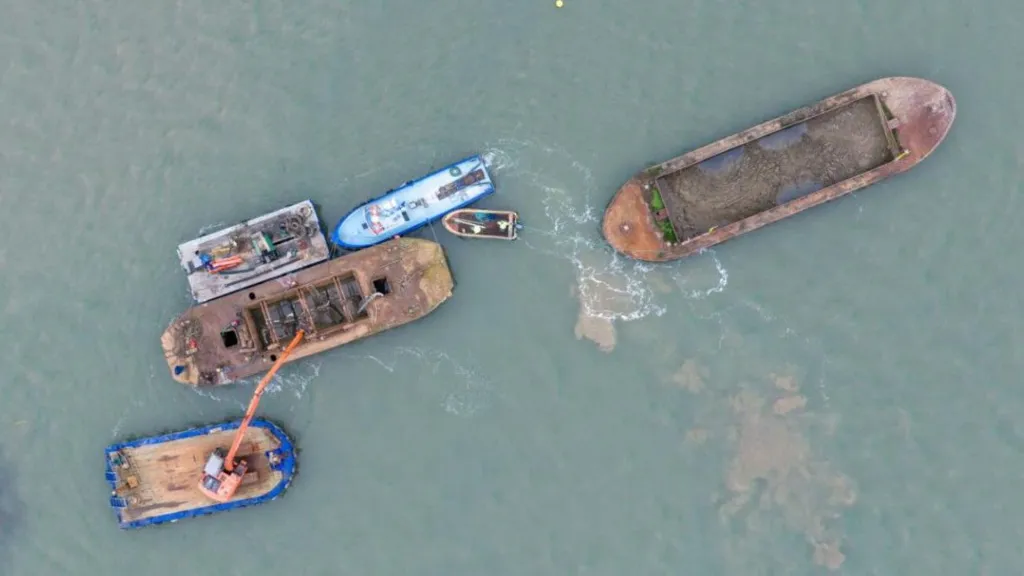 An aerial shot shows two old brown barges and several other vessels on some water
