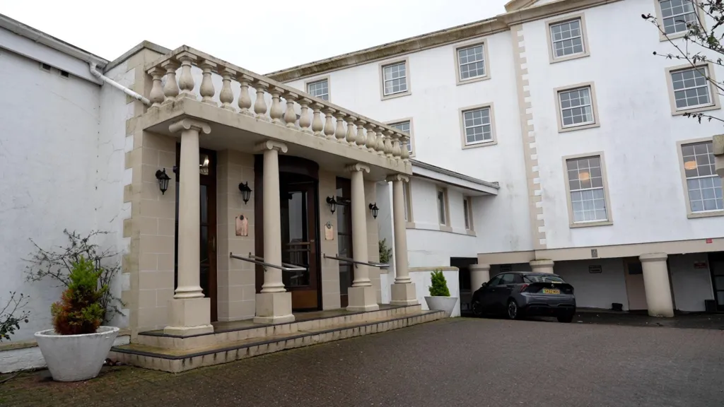 The entrance to the North West Castle Hotel with four beige pillars and decorative spindles, with many rectangular hotel room windows featured in the background 