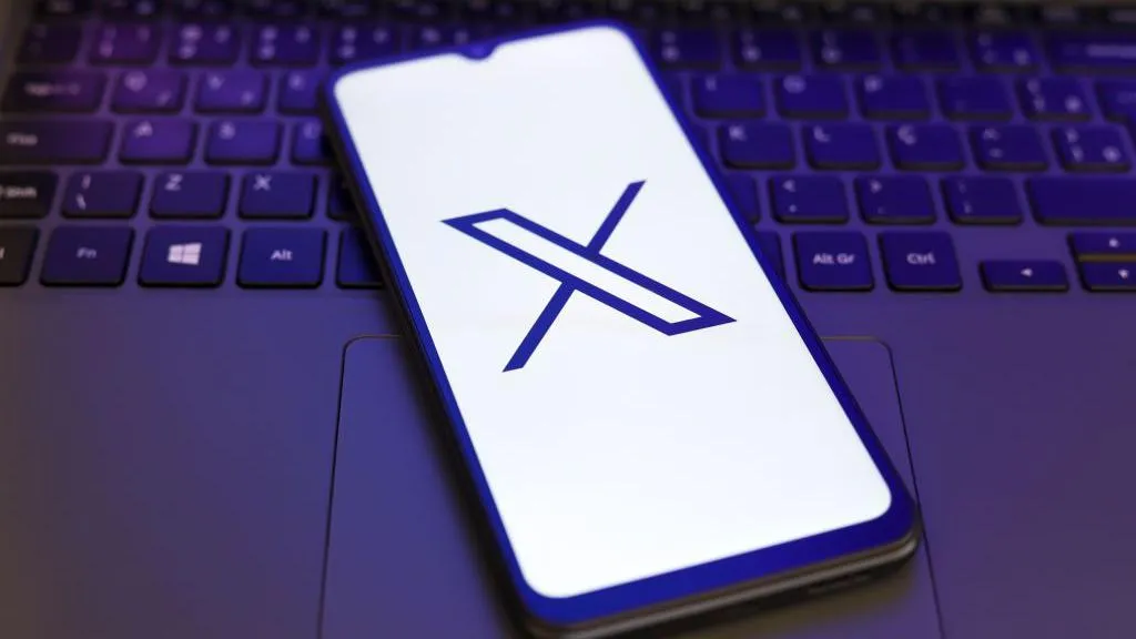 X logo displayed on a smartphone lying on a laptop keyboard