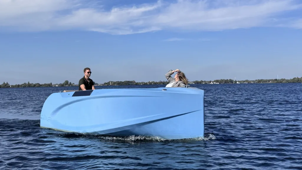 A blue speed boat on a lake with a man in sunglasses at the wheel and a woman at the front.