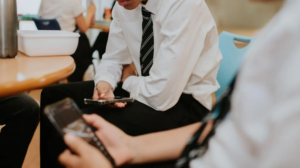 Two boys in uniform look at their smartphones sitting at a wooden table