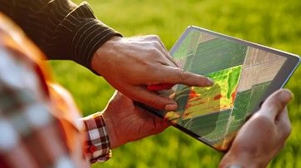 A tablet computer shows a map of a farm with someone pointing to a particular field.