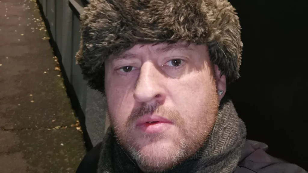 A man, Gary Mooney, wears a fur lined russian hat and looks intensely into the camera 