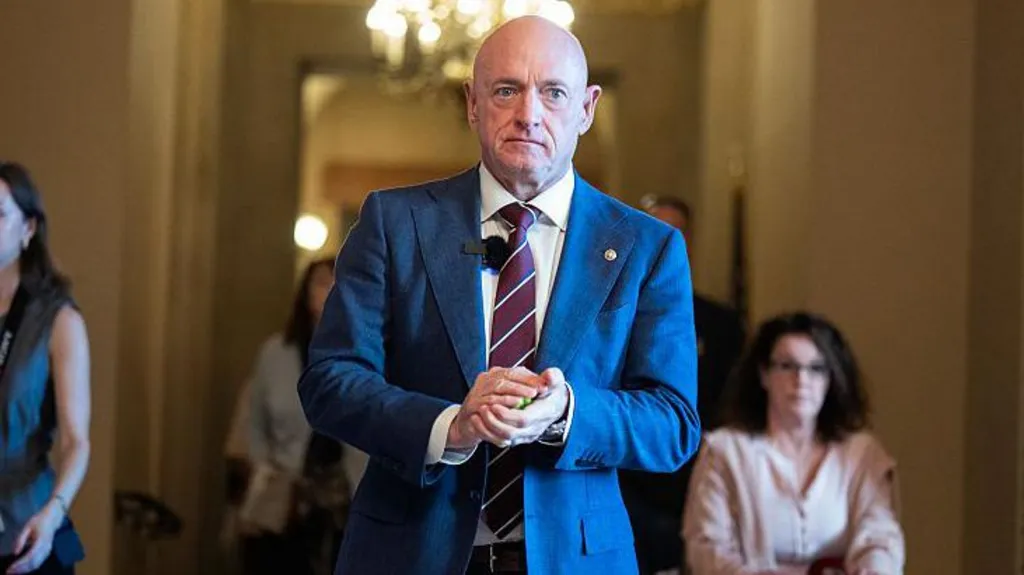 Senator Mark Kelly, wearing a suit, walking forward in a government building hallway with his hands clasped in front of him