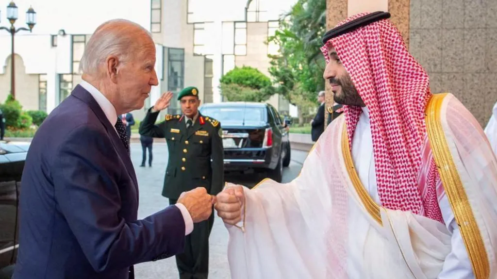 Biden fist bumps with MBS as a security guard salutes in the background.