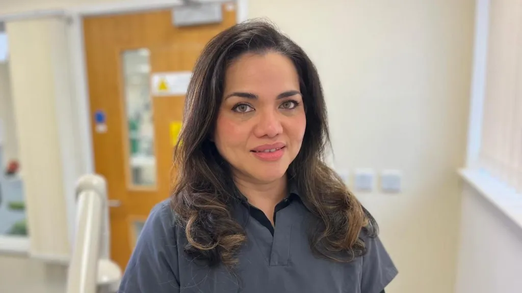 Dr Kanagasingam, who has dark, shoulder-length hair and is wearing blue/grey medical scrubs, is sitting in a laboratory.