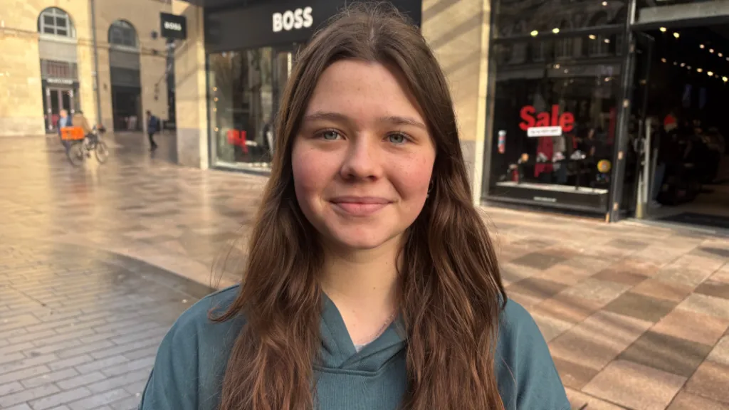 A brunette girl in a blue hoodie smiling at the camera 