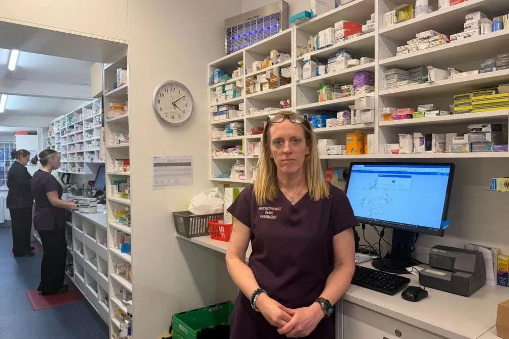 Gwawr Jones stood at a counter in her pharmacy. Shelves holding various items of medication can be seen behind her with colleagues at the pharmacy stood on the left.