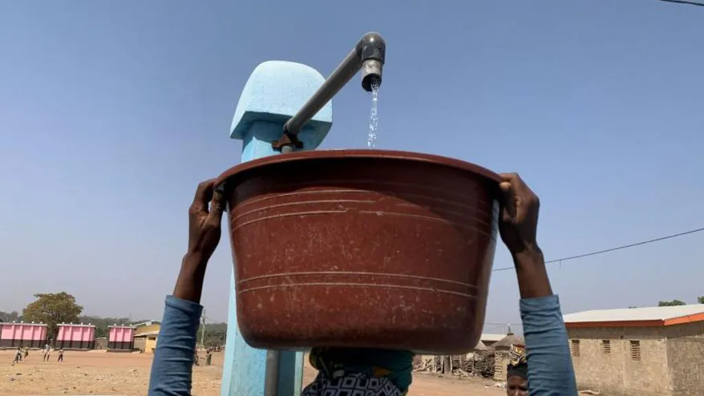 A woman has a bucket on her head, which is being filled with water