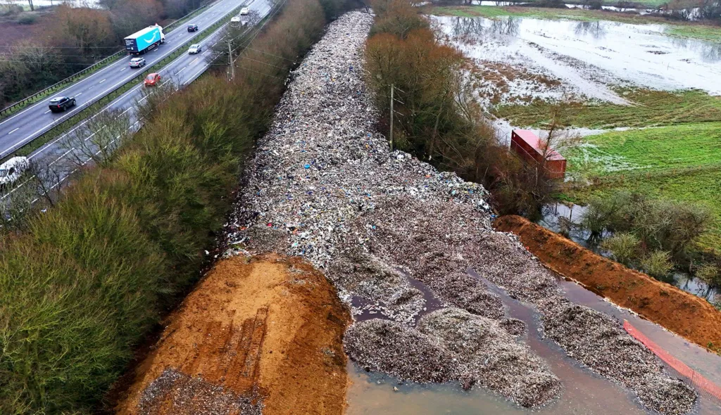 An aerial shot of the dumped waste, stretching out in a road-like line into the distance and surrounded on both sides by trees next to a motorway.