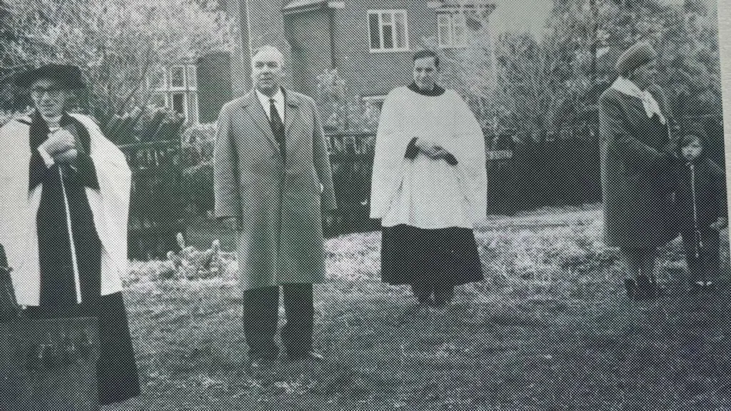 A black and white photograph of the men standing on the verge at the site where the tree is to be planted