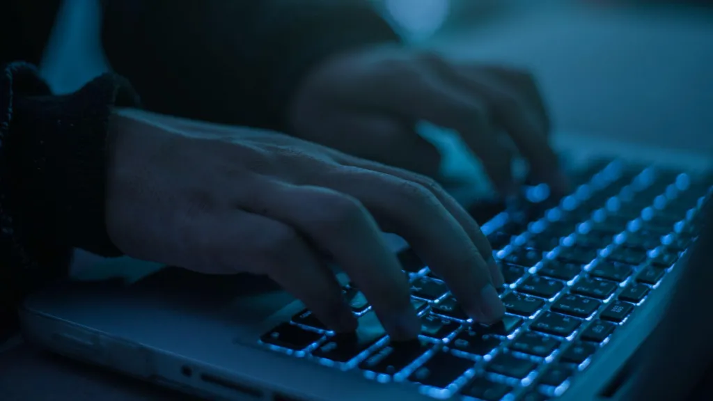 A pair of hands tapping on a computer which is lit with a deep blue light