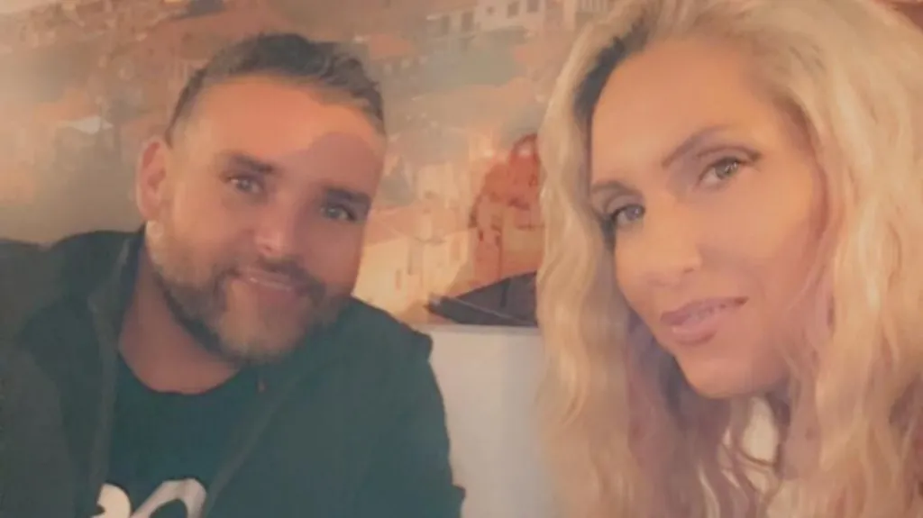 Jessica, who has long blonde hair, smiles in a selfie with her husband Dan, who is wearing a black jumper and has short silvery hair and stubble. It is a head shot of the two of them. 
