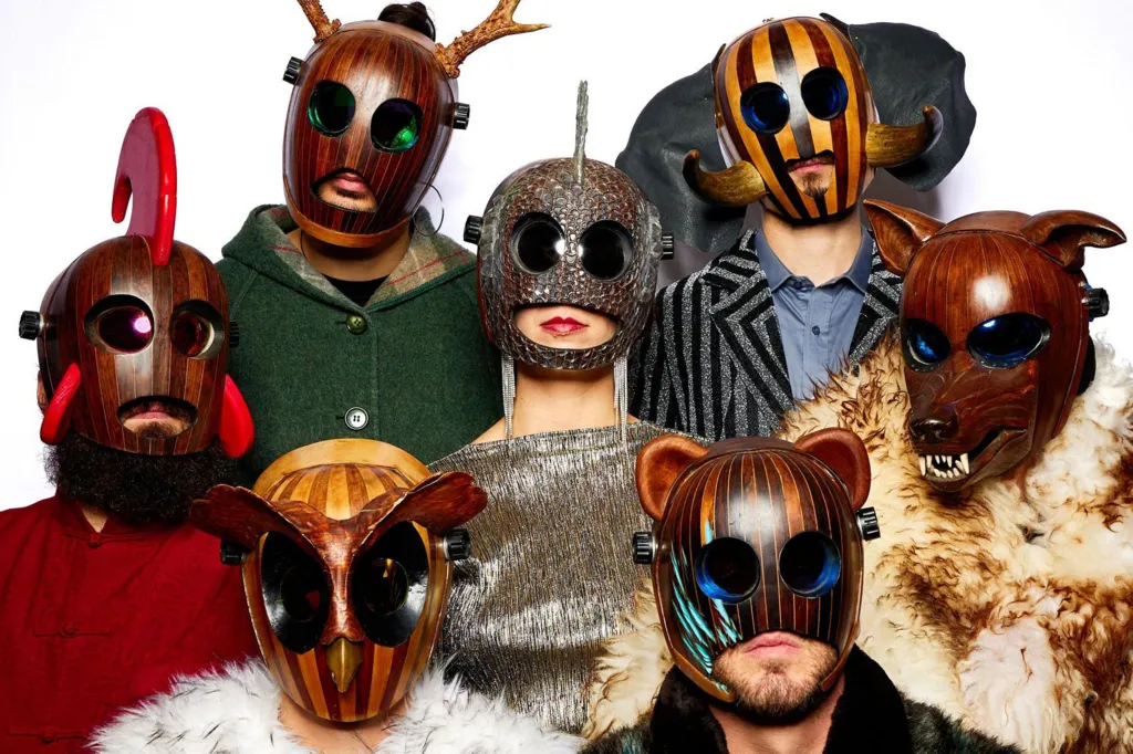 The band FÜLÜ are wearing strange wooden masks, including ones that looks like an owl, a bear and a wolf with big teeth. The band members are standing together and pictured against a white background.