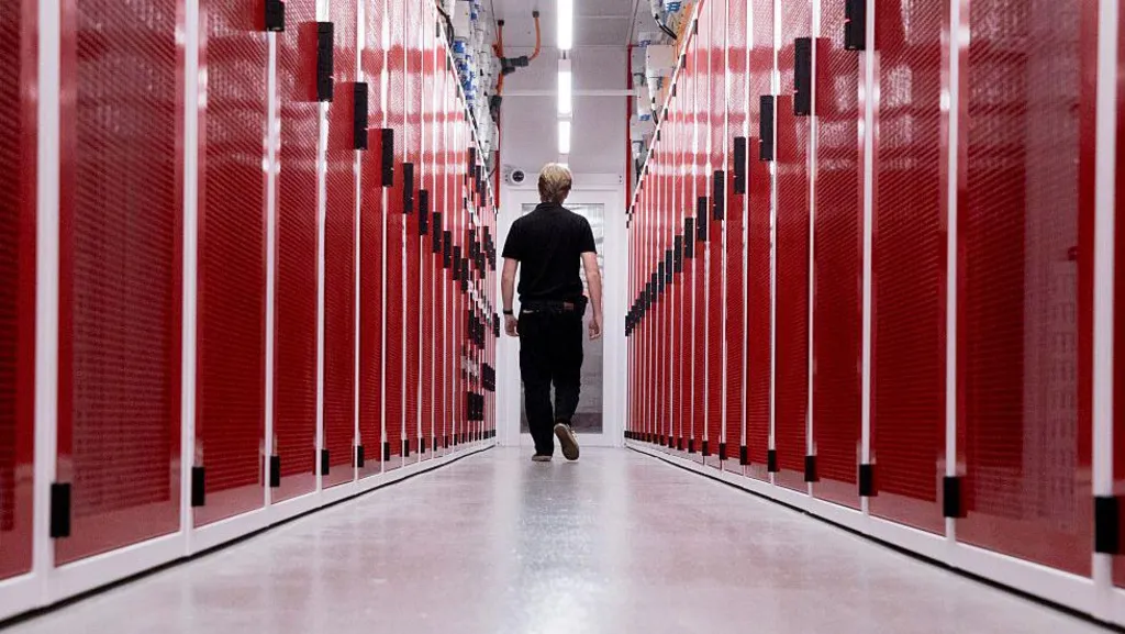 A worker at a data centre in Sydney, Australia, walking down the middle of two rows of red-faced computer servers