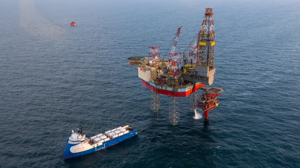 A blue ship sails close to the Siri platform, which looks like an oil rig.