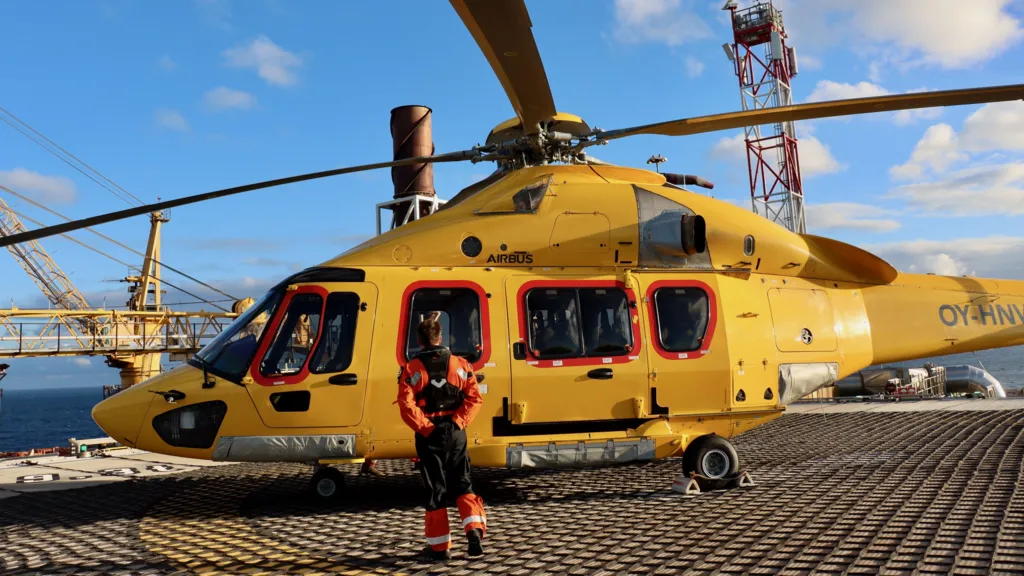 A worker approaches a yellow helicopter, which is sitting on the helipad of an oil platform.