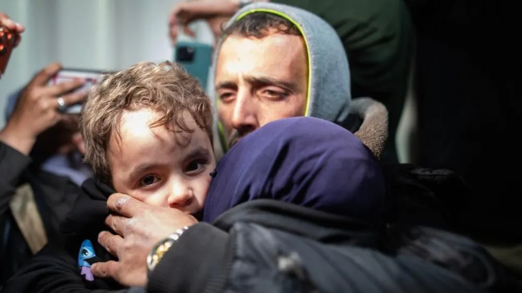 A young Palestinian boy being hugged by adults looks towards the camera at Nasser hospital, in Khan Younis, Gaza, after passing through the Rafah crossing with Egypt (2 February 2026)