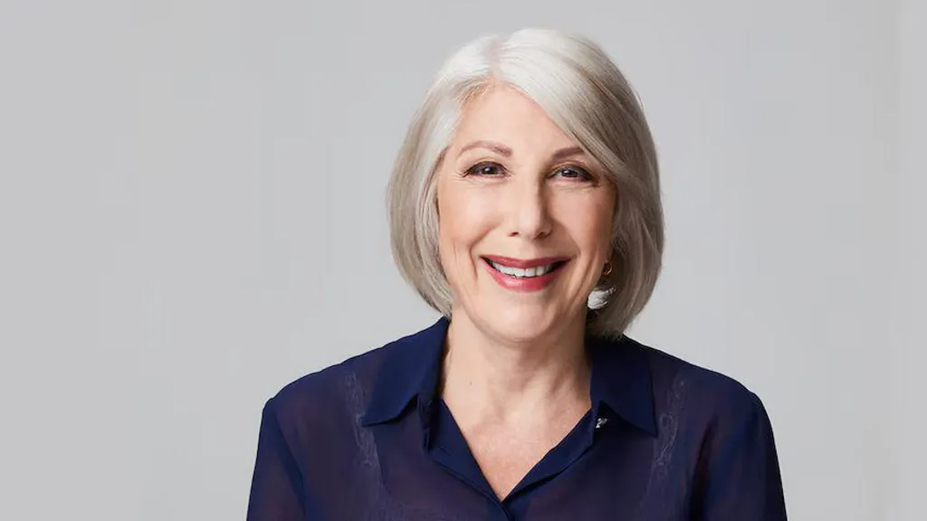 An older woman with grey hair smiles at the camera.
