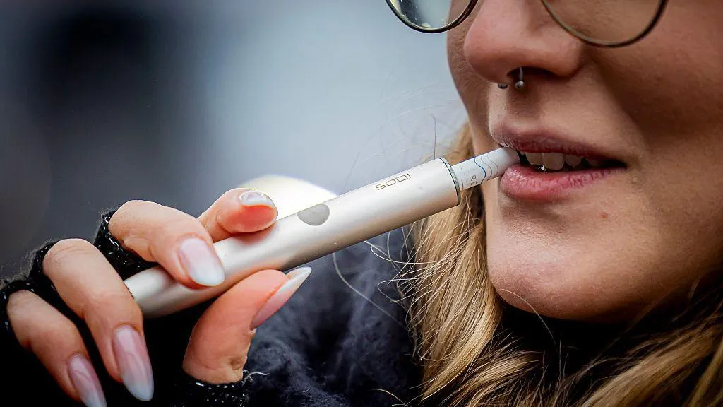 A woman uses a silver vape and put its to her mouth