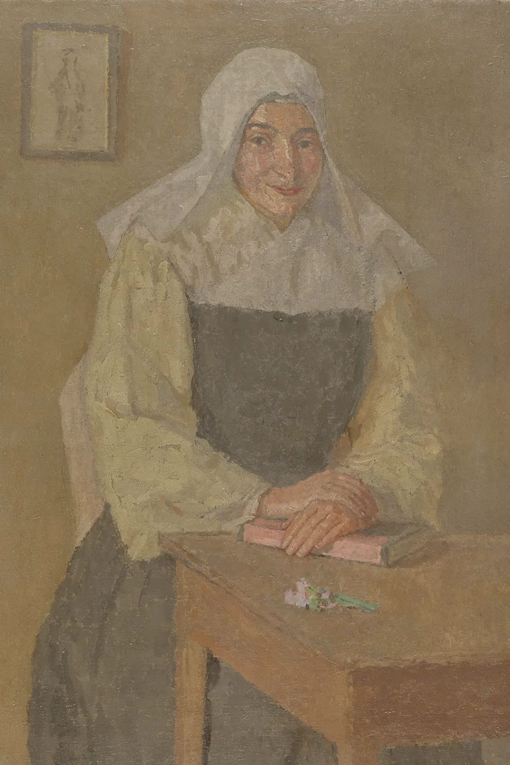 Oil painting of a nun seated at a table with her hands crossed over a book lying on it. She wears a white veil, a cream coloured blouse and a black pinafore style long dress. She is smiling slightly to the left of the painting. There is a picture of a figure on a wall behind her.