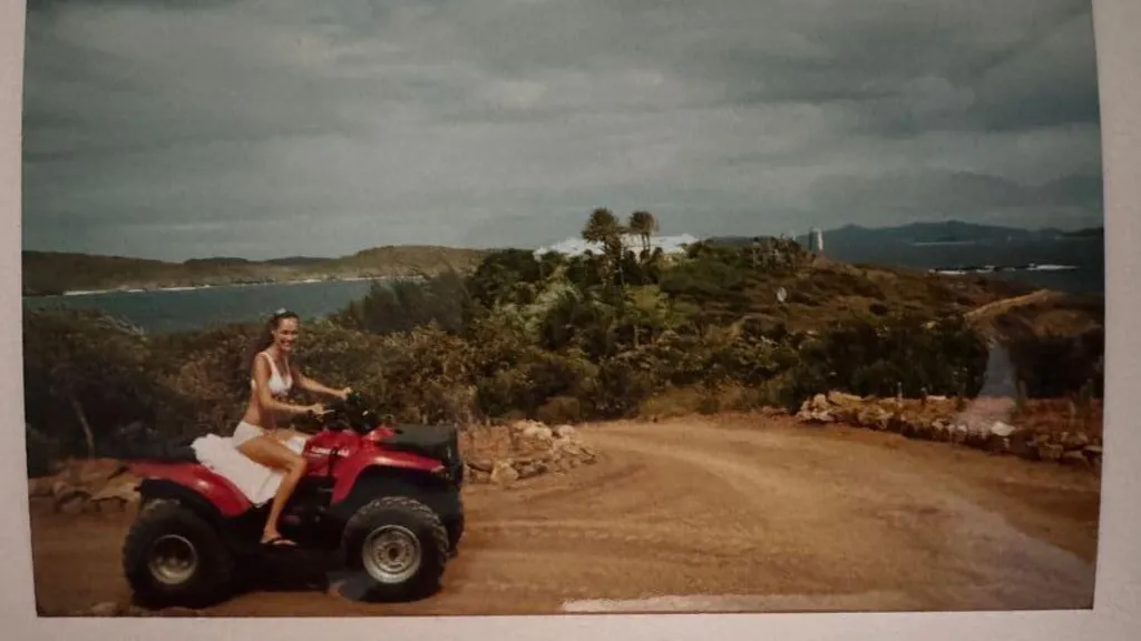 A photograph of a photo of Juliette wearing a white bikini and flip flops while  on a quad bike on Epstein's island in 2002 