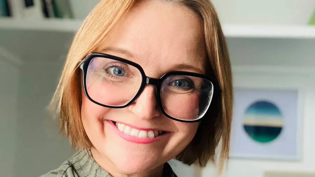 A woman with glasses smiling at the camera. It is a head shot of her.
