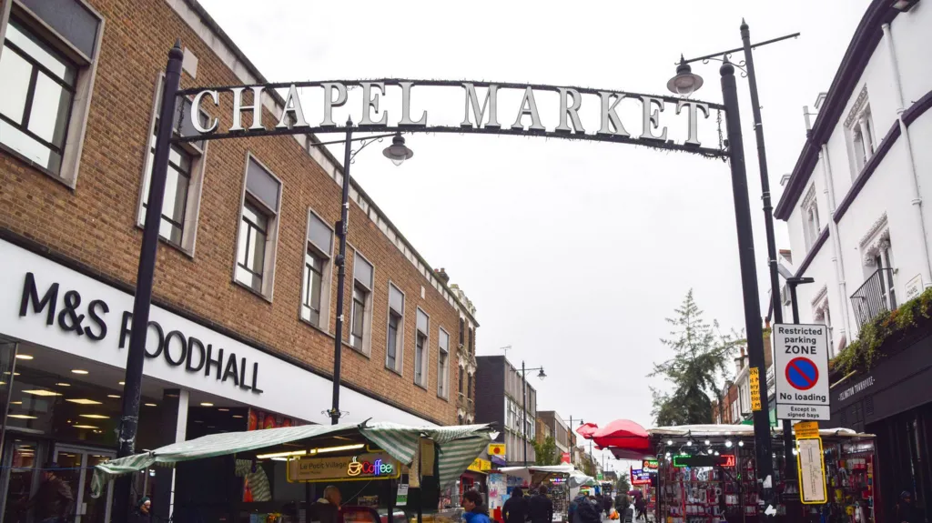 A road with stalls in. A large sign sits over the top reading "Chapel Market".