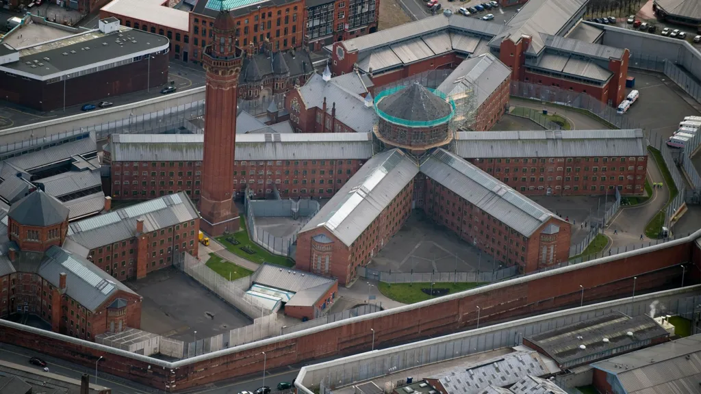 Red-brick prison building - with various wings emerging from a central tower. There is another much taller tower to the left of the image - and a high perimeter walls encircling the complex.