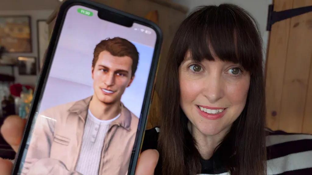 Journalist Nicola Bryan is holding up her mobile showing her AI avatar George. Nicola has long dark hair with a fringe and is wearing a black and white striped jumper. George has short auburn hair, a beige open jacket and a white granddad collared top on underneath, Both are smiling at the camera. 
