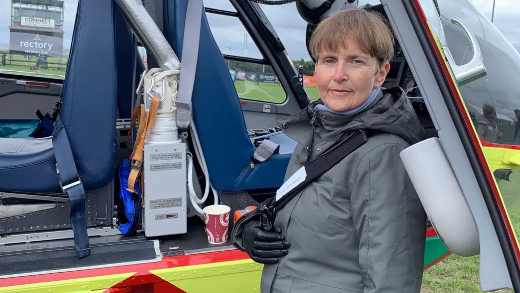 Helen Hide-Wright with her arm in a sling stood by an air ambulance. 