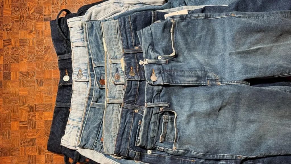 Six pairs of denim jeans stacked on top of each other.