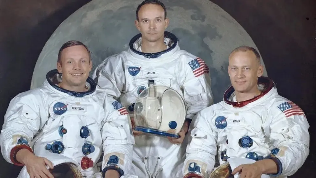 Official portrait of the Apollo 11 crew Neil Armstrong, Michael Collins and Buzz Aldrin, dressed in their spacesuits, taken against the backdrop of an image of the Moon