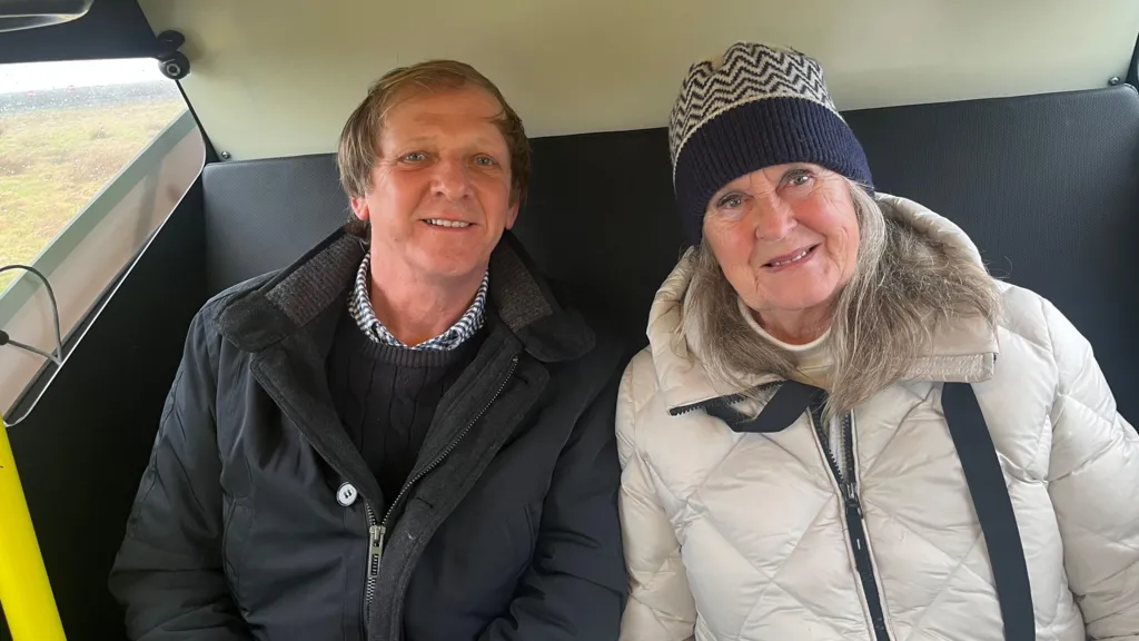 A man with a black jacket and a woman with a white jacket and blue and white hat sitting on a seat next to each other.