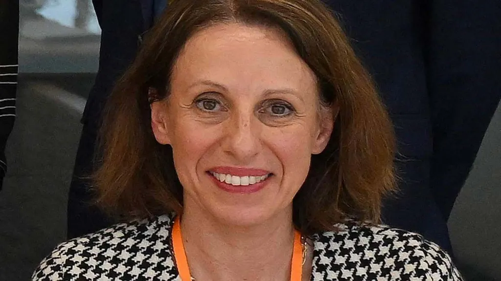 Shirine smiles while wearing a black and white houndstooth jacket and an orange lanyard.