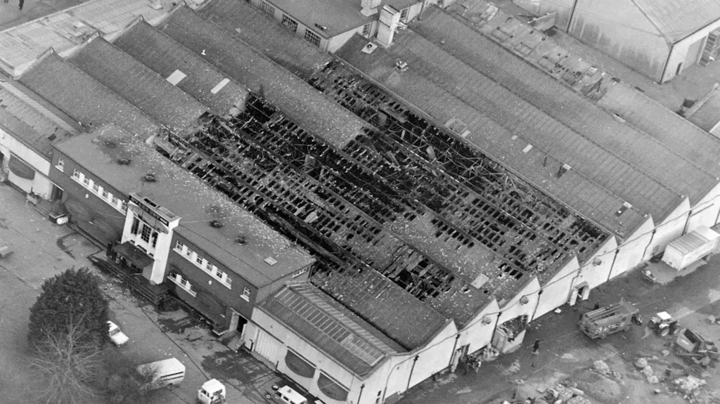 A black and white aerial shot of Stardust nightclub after the fatal fire.  The large, warehouse-like complex consists of several attached buildings with pitched roofs and a main entrance with a flat roof and large windows.  More than a third of the pitched roofs are badly burned, with damaged rafters visible.