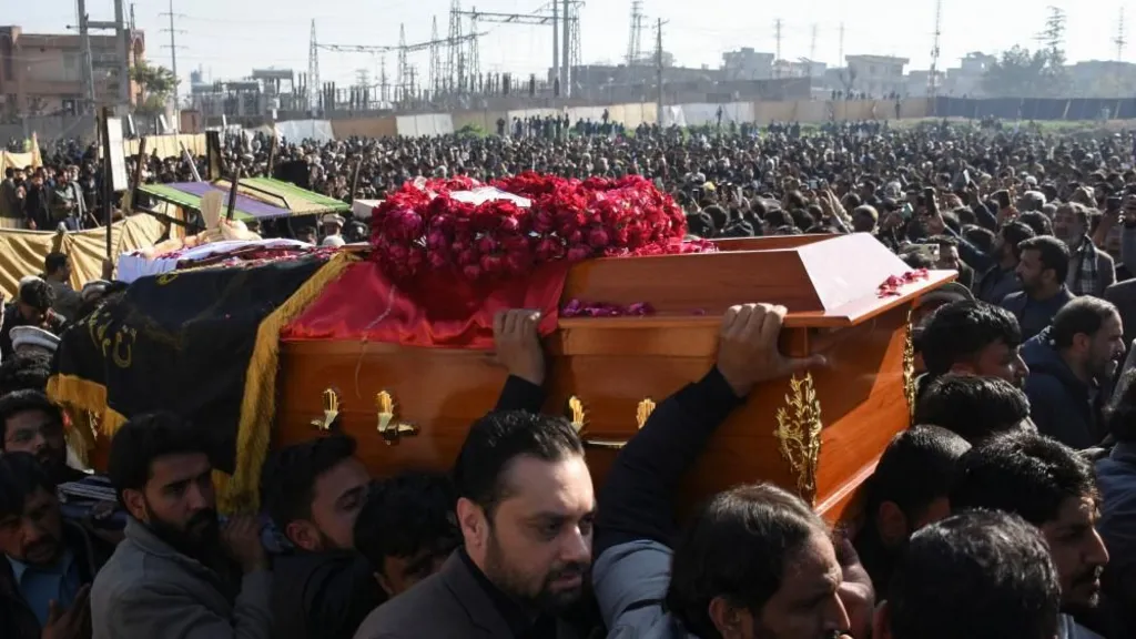 Several men carry a coffin through a huge crowd