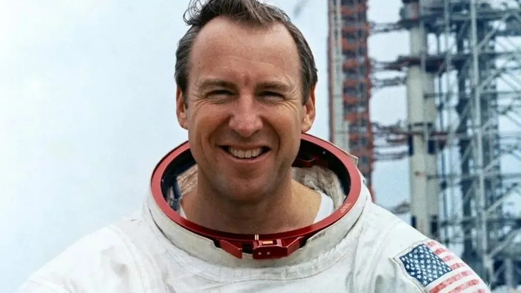 Jim Lovell grins as he stands in front of a launchpad dressed in his spacesuit while training for the Apollo 13 mission