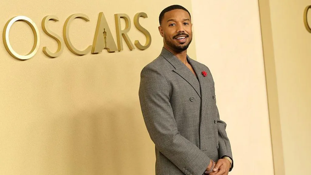 Michael B Jordan seen walking on the red carpet at the annual Academy Awards luncheon in Los Angeles. The Oscars logo is seen behind him on a yellow wall. 