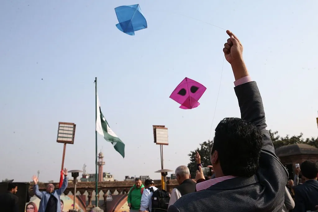 A man lets off a kite during the Basant kite festival in Lahore, Pakistan, as seen from behind him with his hand in the air and the kites flying off in the blue sky.