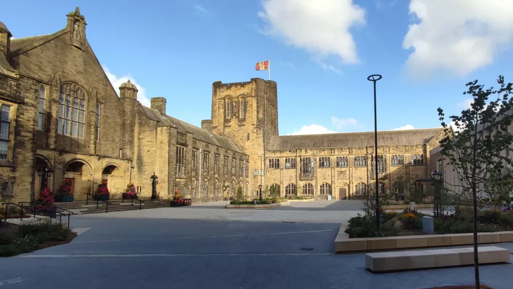 The main university site at Bangor:  a large, historic stone building and mullioned windows and a crenallated tower in the corner 