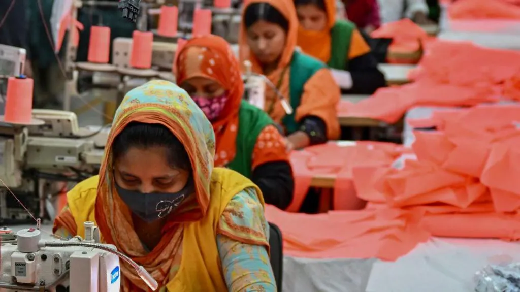 A picture of women making clothes in an assembly line in Bangladesh. The women are pictured in a row with their heads down as they use sowing machines