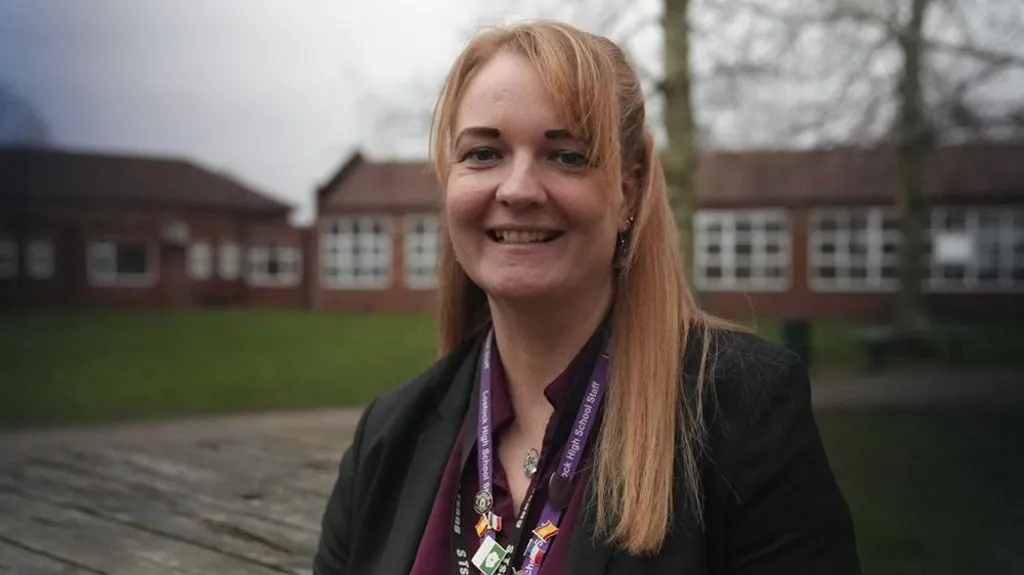 Samantha, who has long blond hair, smiles at the camera wearing a burgundy shirt and black jacket. 
