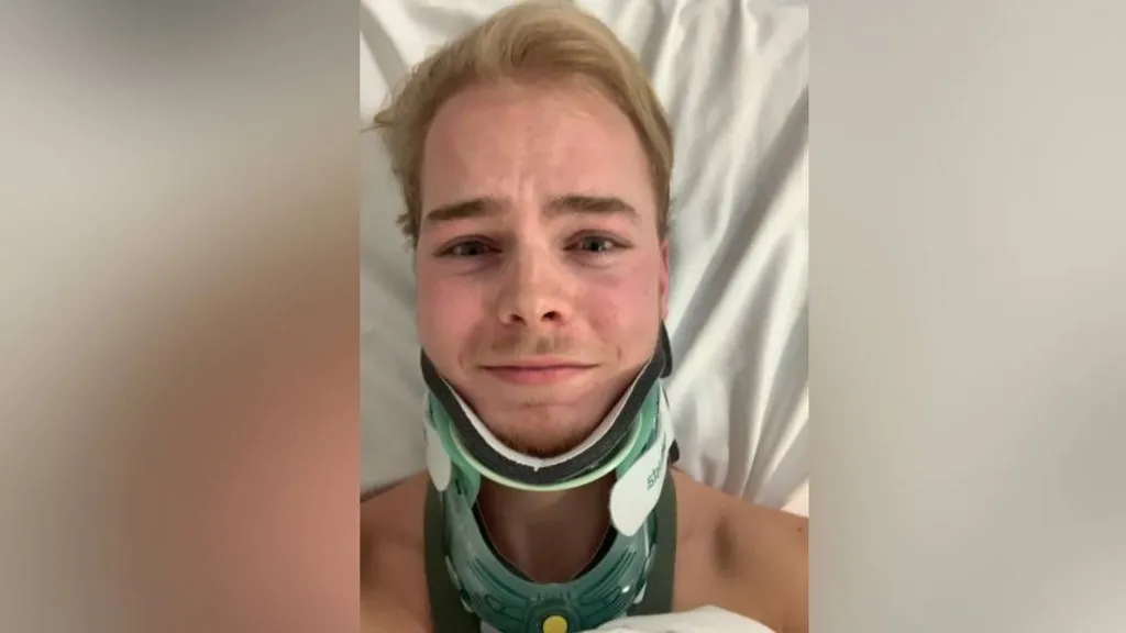 A selfie of Ellis Pears in hospital wearing a green neck brace. He has short blond hair and his chest is covered with a white hospital sheet.
