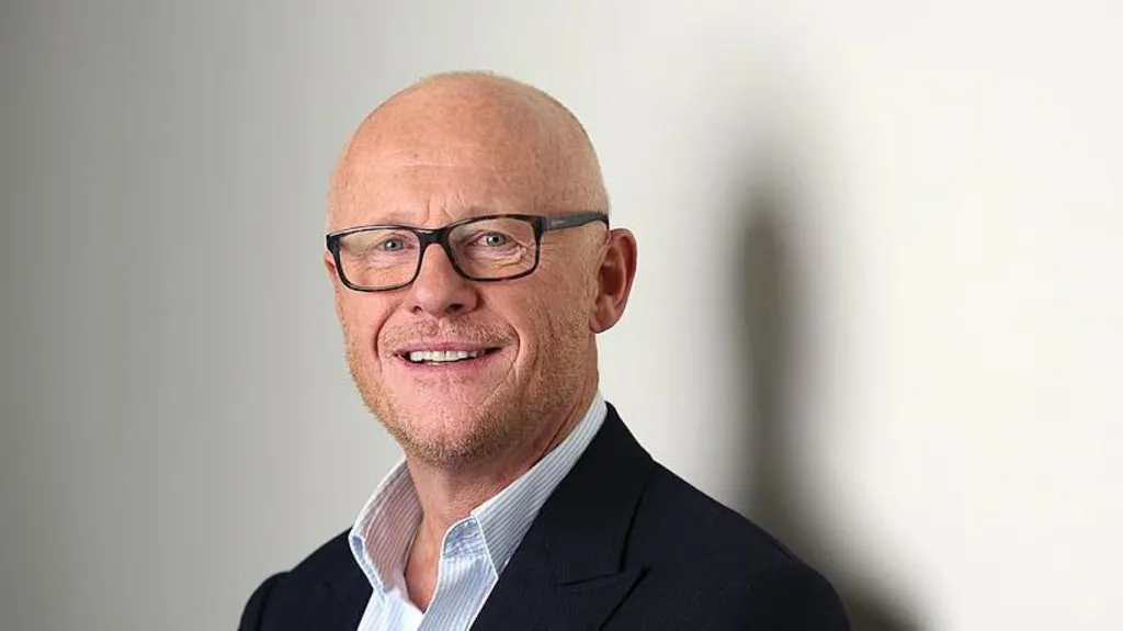 Billionaire Phones4U founder John Caudwell, wearing a black suit and white striped shirt and glasses