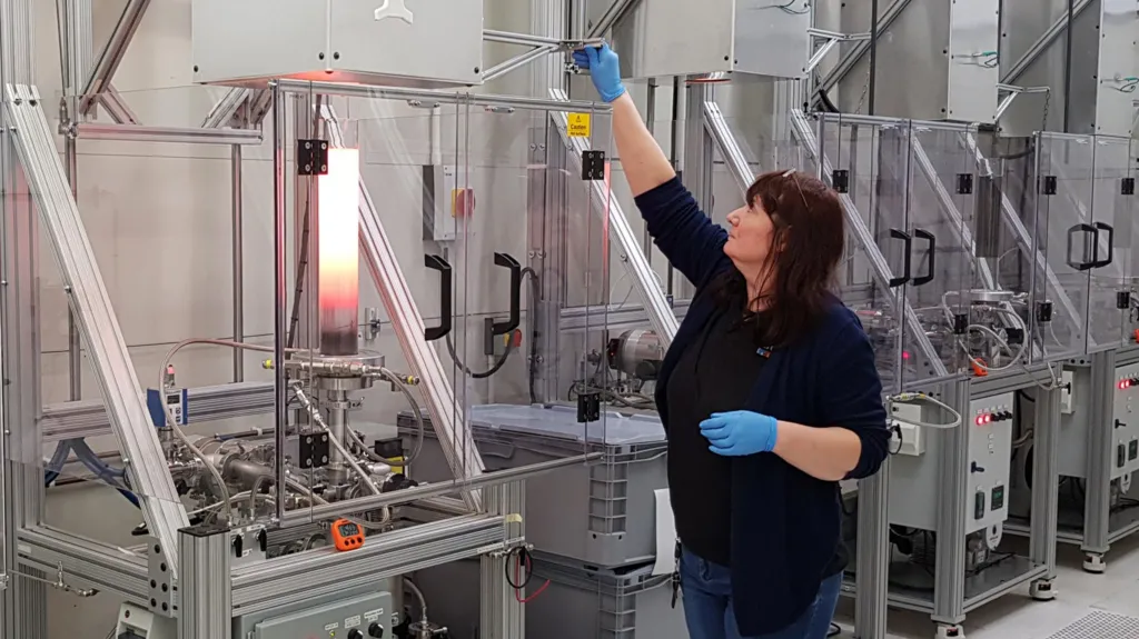 A technician wearing blue gloves adjusts one of a line of furnaces.